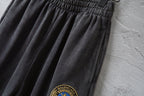 Dark gray wide-leg pants with embroidered crest patch near the hem