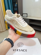 Gold and white low-top sneakers with white laces, ornate upper, gold logo badge on side