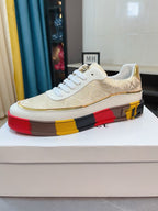 White and gold low-top sneakers with gold-pattern upper and white laces, red yellow black sole