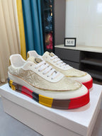 White and gold low-top sneakers with ornate upper, white laces, bold red yellow platform sole