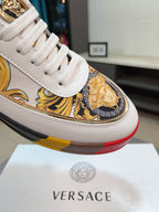 White luxury sneakers close-up with gold baroque print and cushioned platform sole.