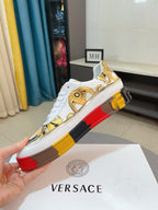 White luxury sneakers side view with gold upper print and red/yellow platform sole.