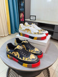 Pair of luxury sneakers—white and black with gold prints and red/yellow platform soles.