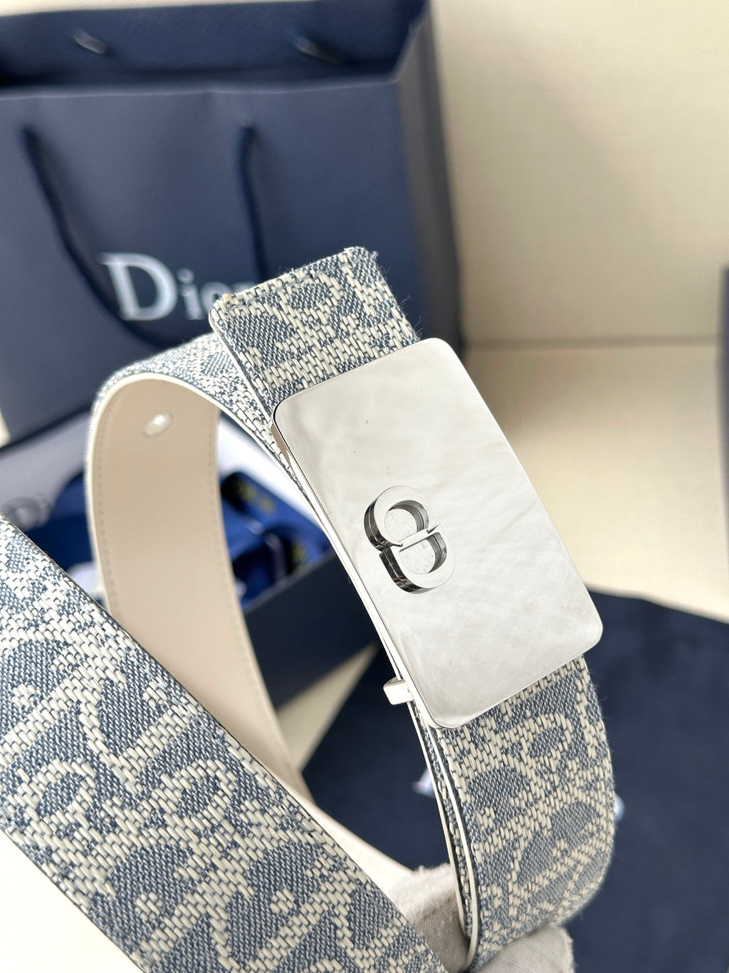 Dior belt close-up: blue monogram strap with silver D buckle and white strap