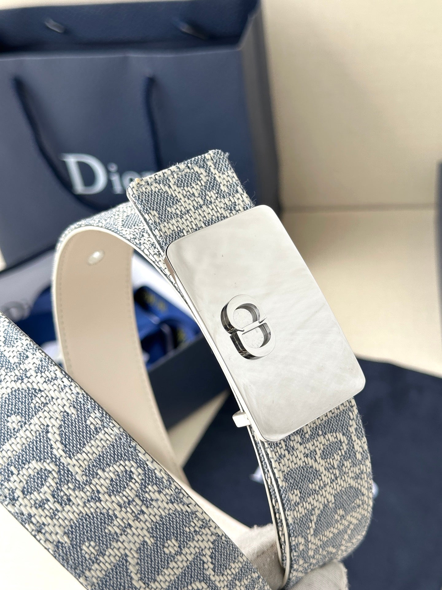 Dior belt close-up: blue monogram strap with silver D buckle and white strap