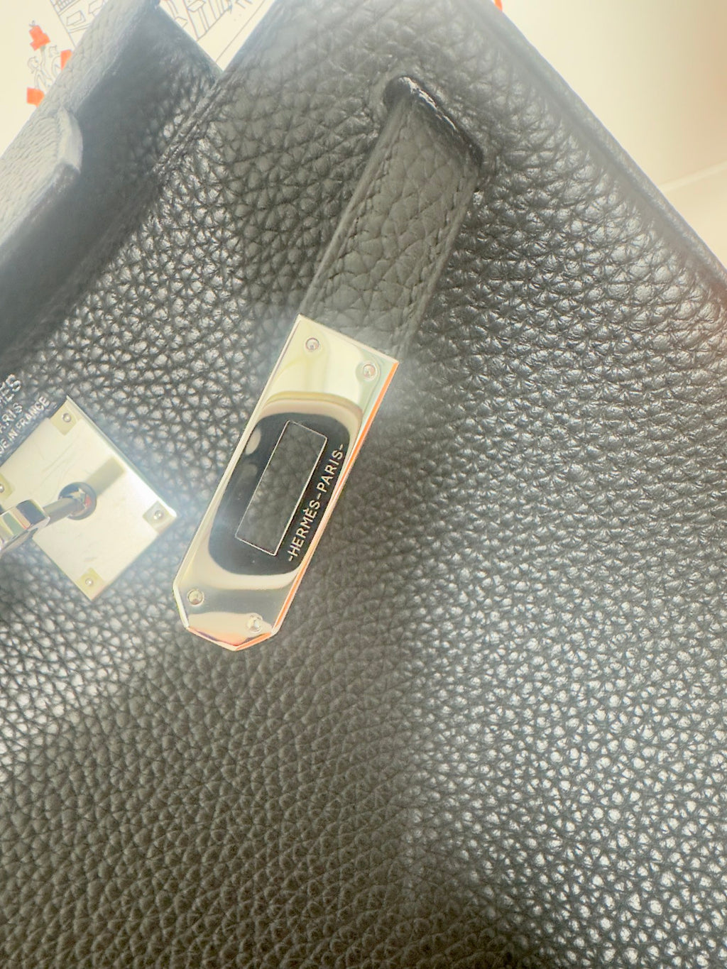 Hermes handbag close-up of dark textured leather surface with brand tag on flap area.