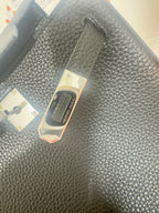 Hermes handbag close-up of dark textured leather surface with brand tag on flap area.
