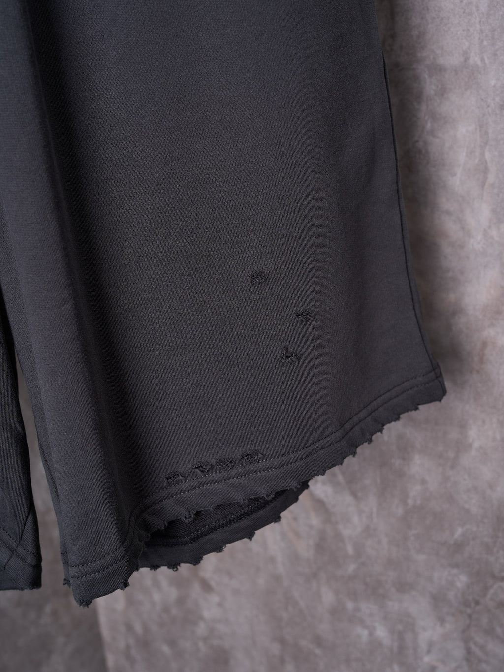 Black shorts side seam closeup with small logo and scalloped lace-trim hem.
