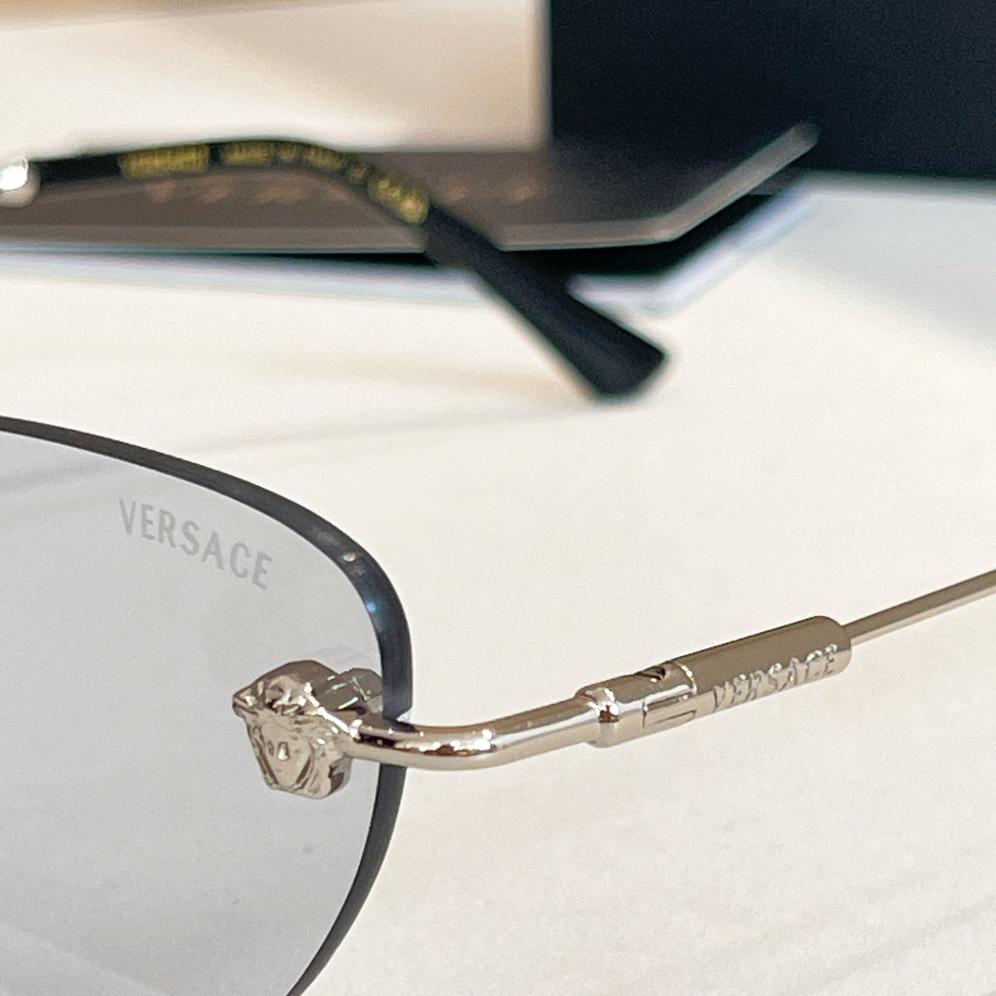 Versace glasses close-up: round dark lenses with black front and gold temple arm