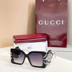 Square black sunglasses with dark lenses and gold logo on side arms