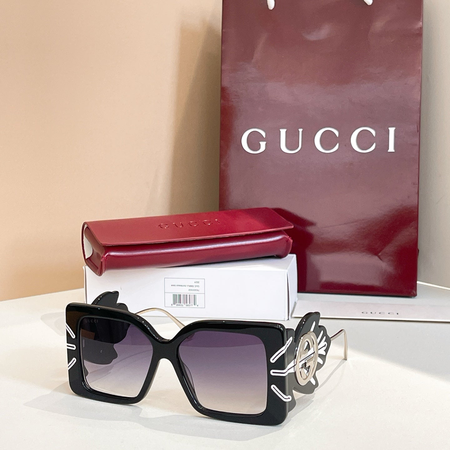 Square black sunglasses with dark lenses and gold logo on side arms