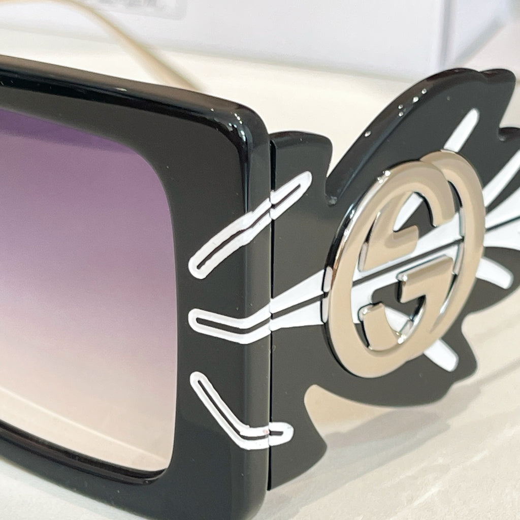 Close-up square sunglasses frame with dark lenses and gold logo on side