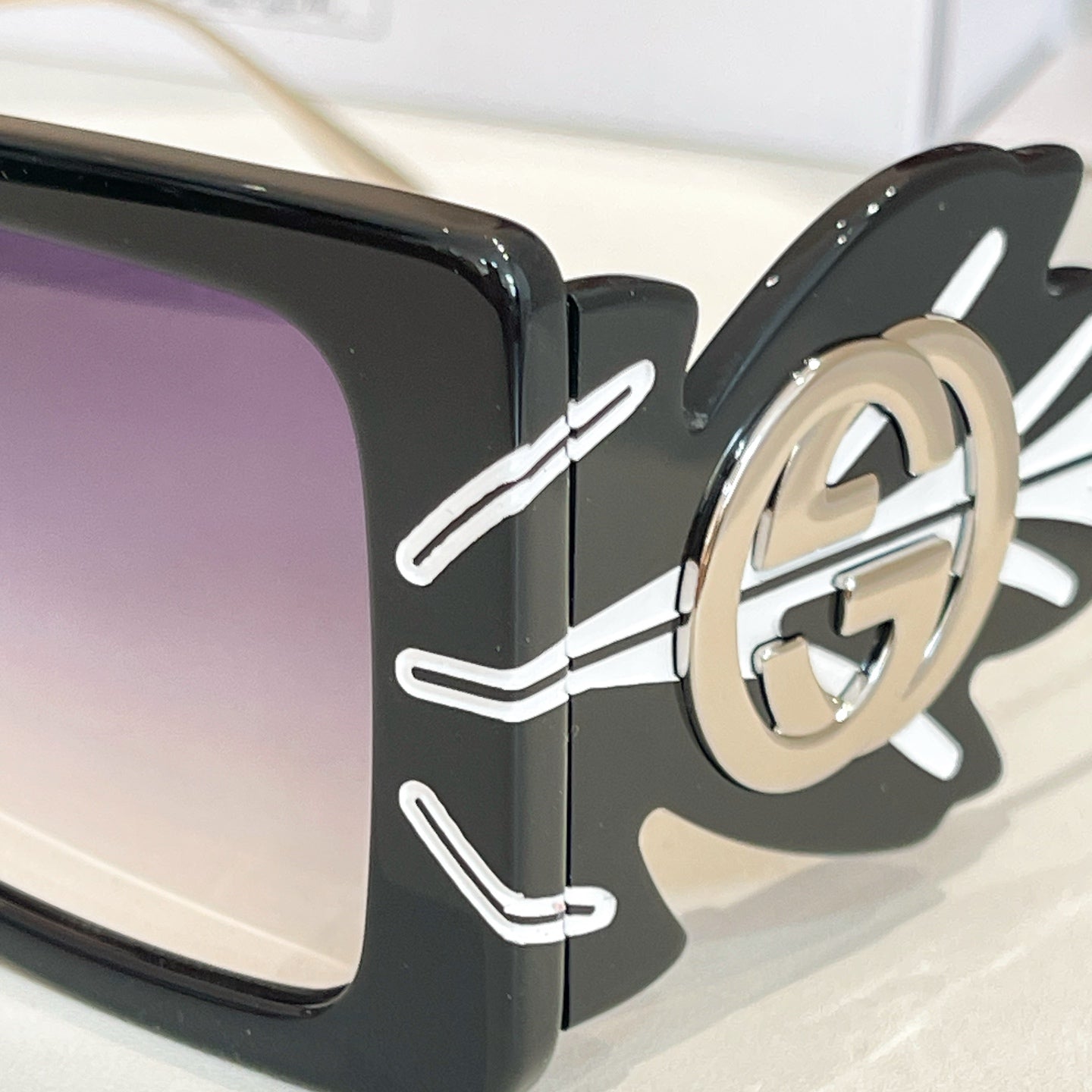 Close-up square sunglasses frame with dark lenses and gold logo on side
