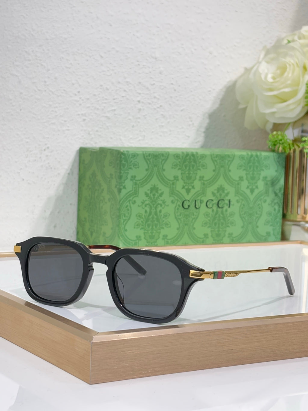 Black rectangular eyeglasses with dark tinted lenses and gold-toned logo arm detail.