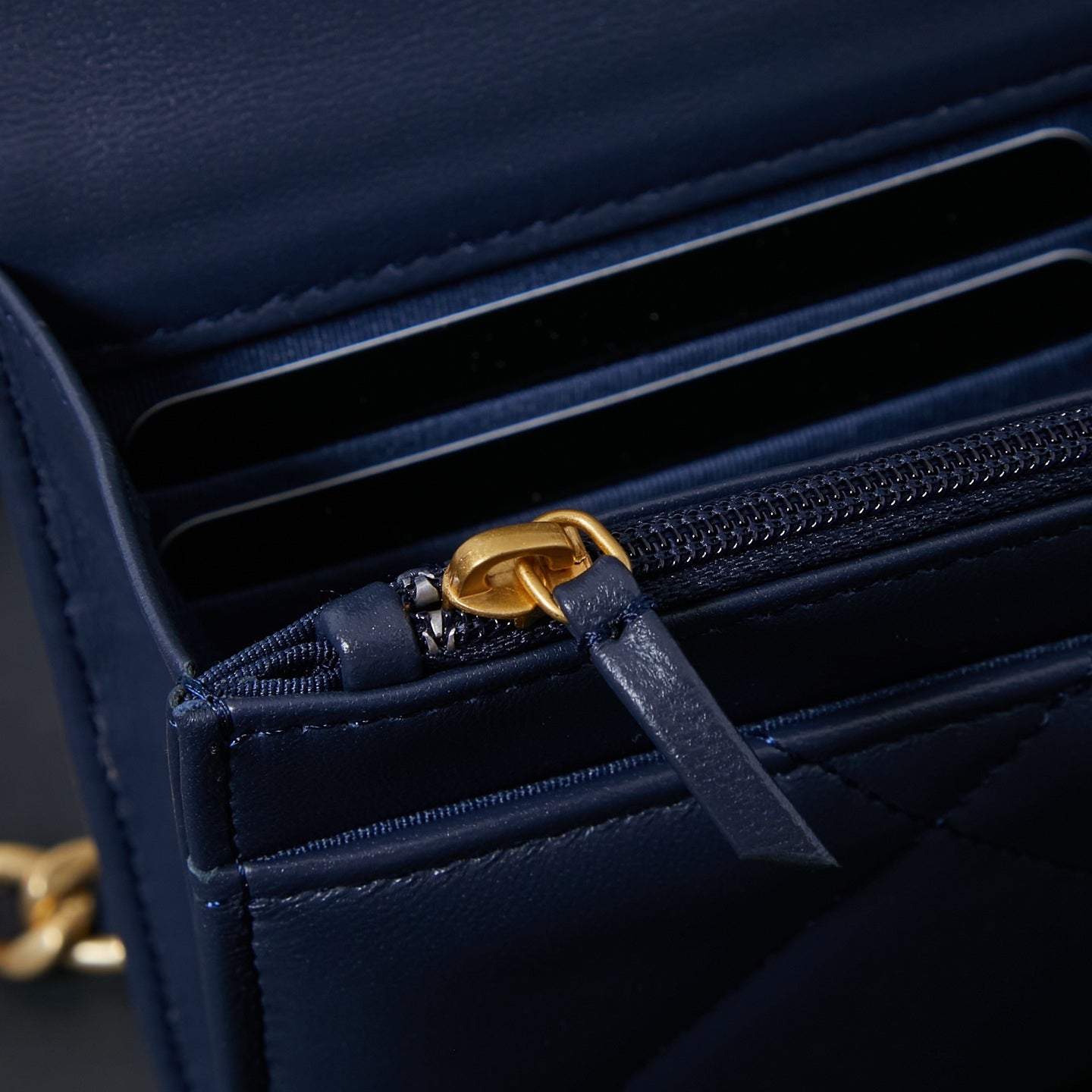 Chanel interior close-up with navy lining and gold chain pull on zipper.