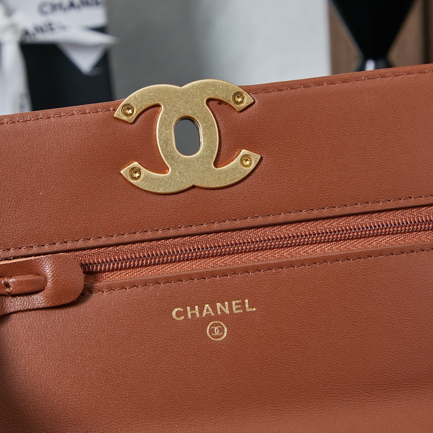 Chanel bag close-up of gold CC logo, tan-brown flap, and zipper trim