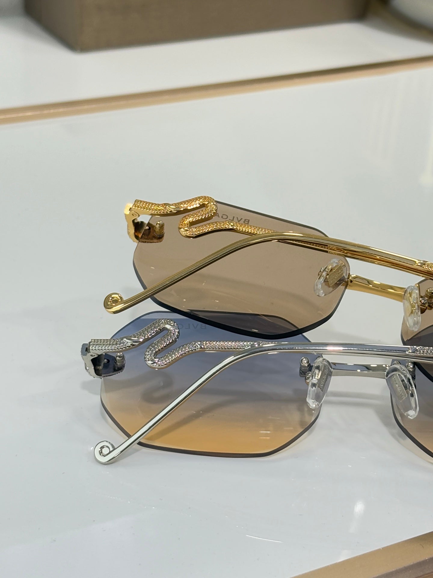 Bvlgari sunglasses close-up: gold-tone frame, beige lenses, rhinestone emblem