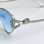 Blue-tinted cat-eye glasses close-up with green jeweled bridge and metal hinges