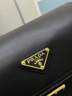 Black leather bag close-up with gold Prada logo plate on the flap