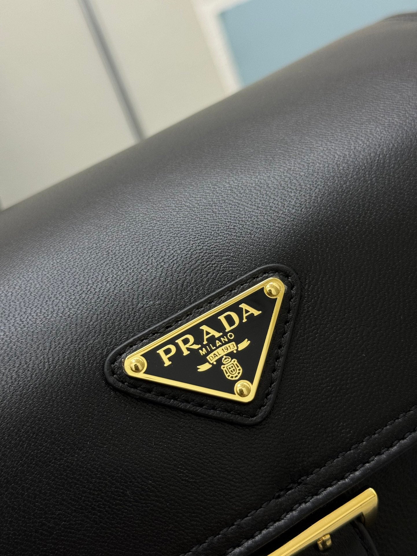 Black leather bag close-up with gold Prada logo plate on the flap