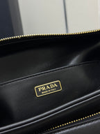 Black leather bag close-up with gold-tone Prada logo patch and zipper edge