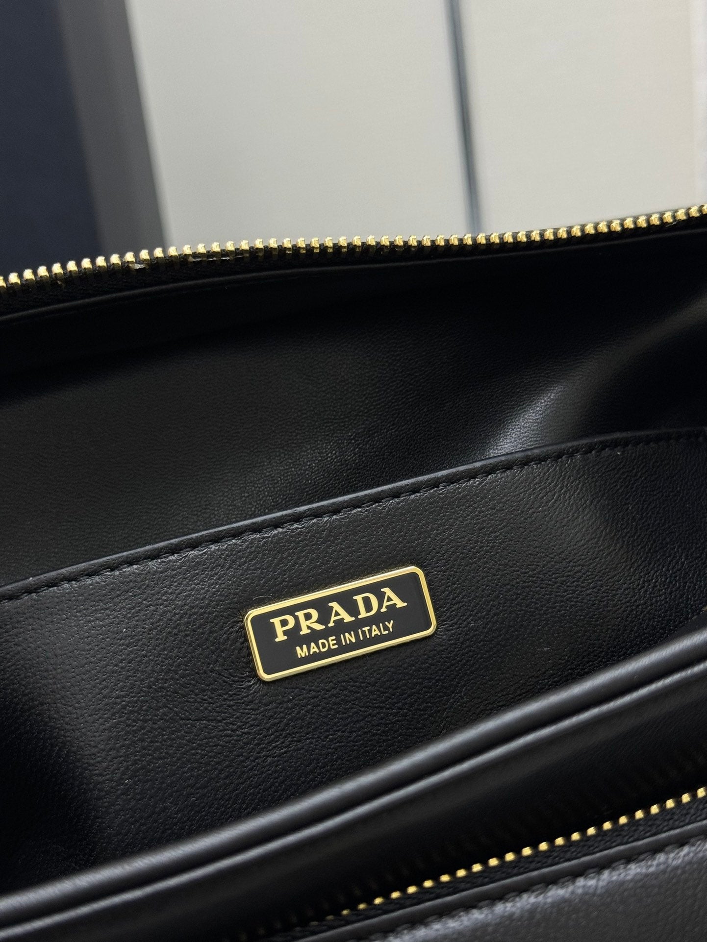Black leather bag close-up with gold-tone Prada logo patch and zipper edge