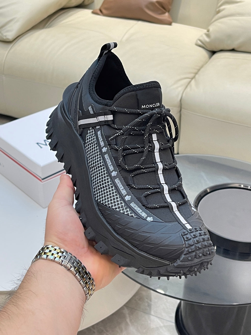 Black Moncler lace-up sneakers held in hand, with mesh side stripe details