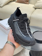 Black Moncler lace-up sneakers held in hand, with mesh side stripe details