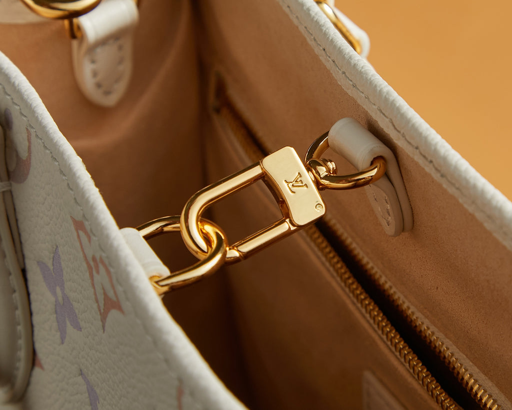 Gold-tone clasp on white monogram tote bag near zipper opening