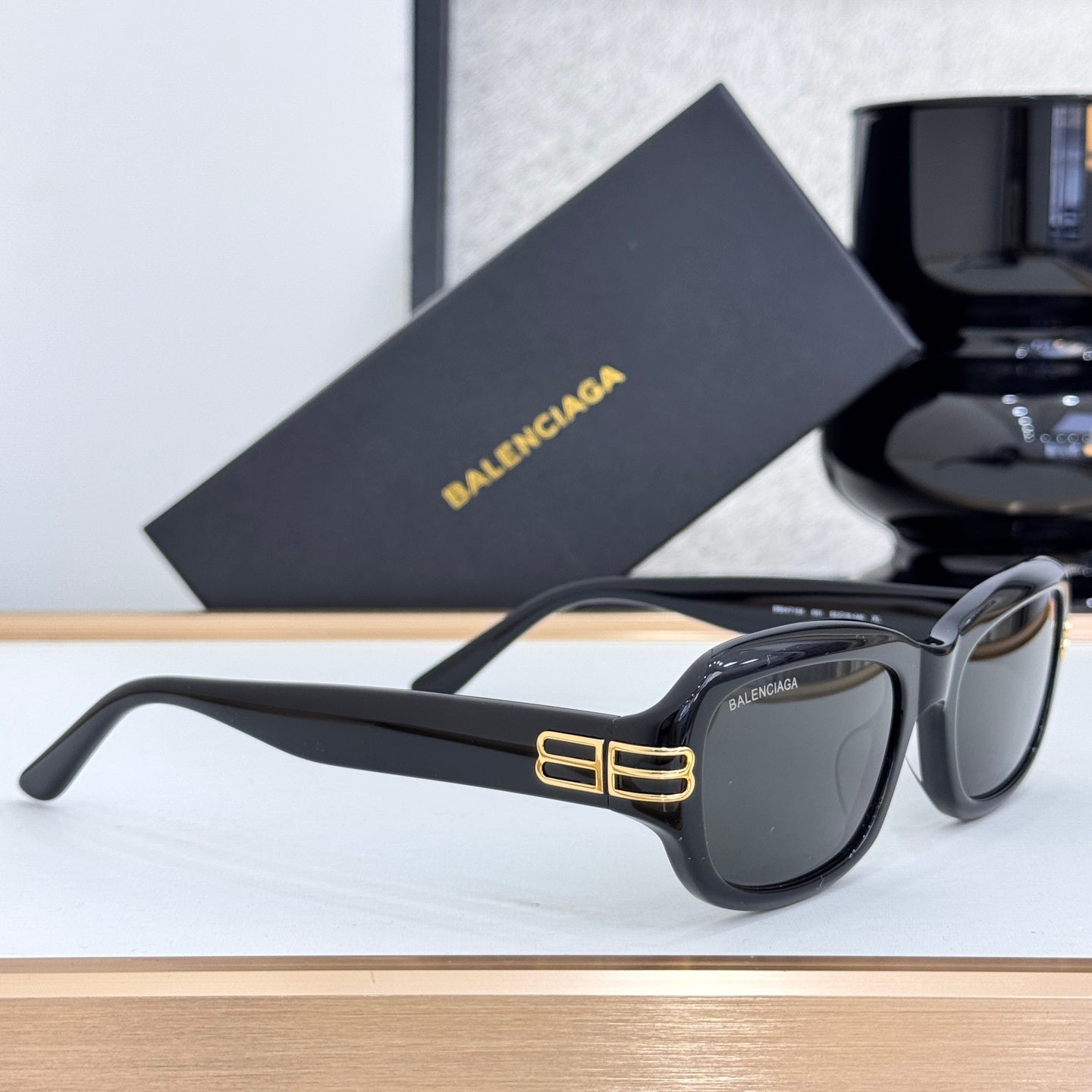 Balenciaga sunglasses in black with dark lenses, side view, gold temple logo