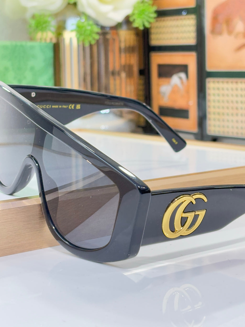 Gucci sunglasses close-up with dark blue frames, dark lenses, and gold G logo on temple