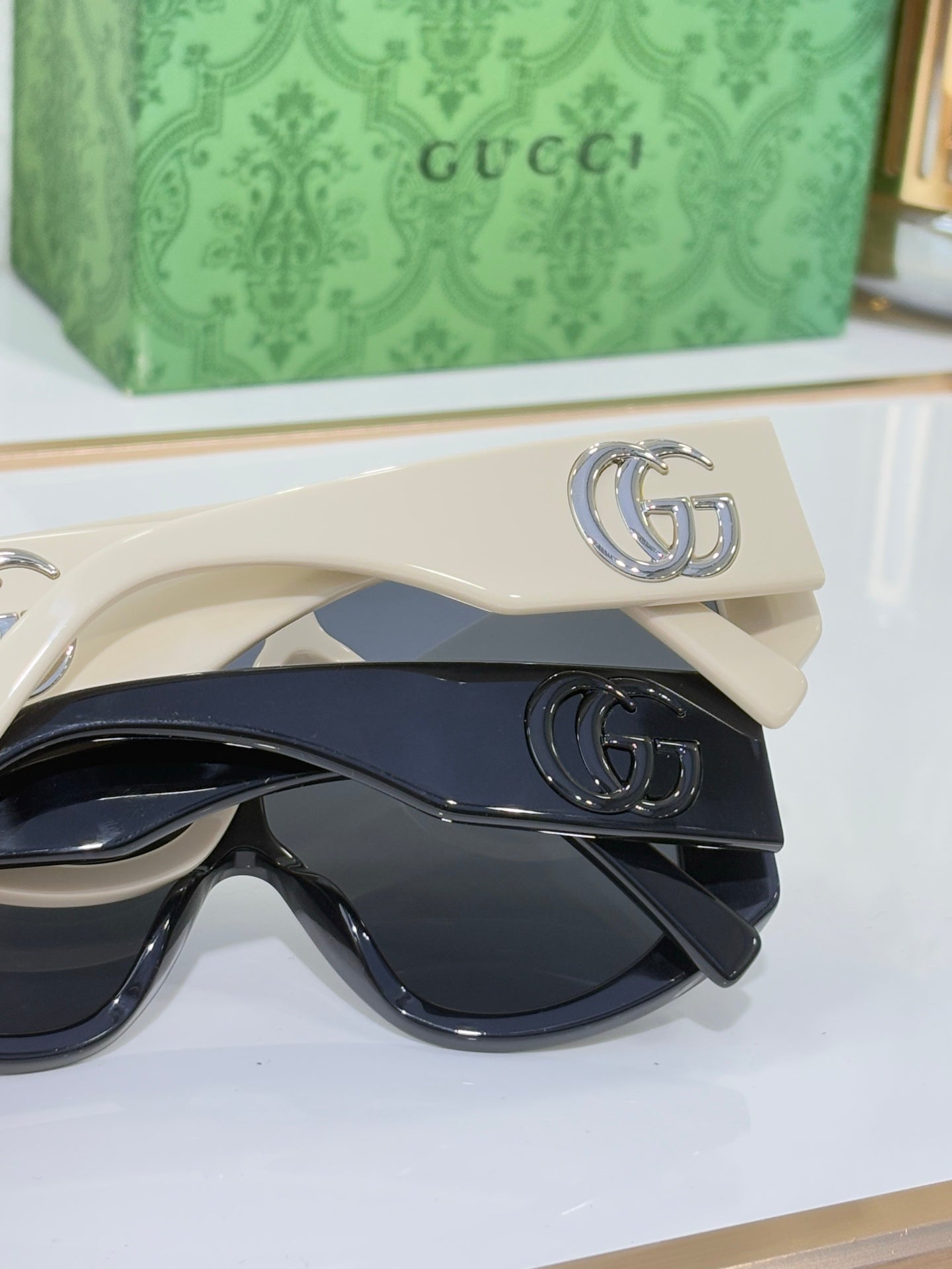 Gucci sunglasses close-up with cream frames, stacked dark lenses, and metal G logo