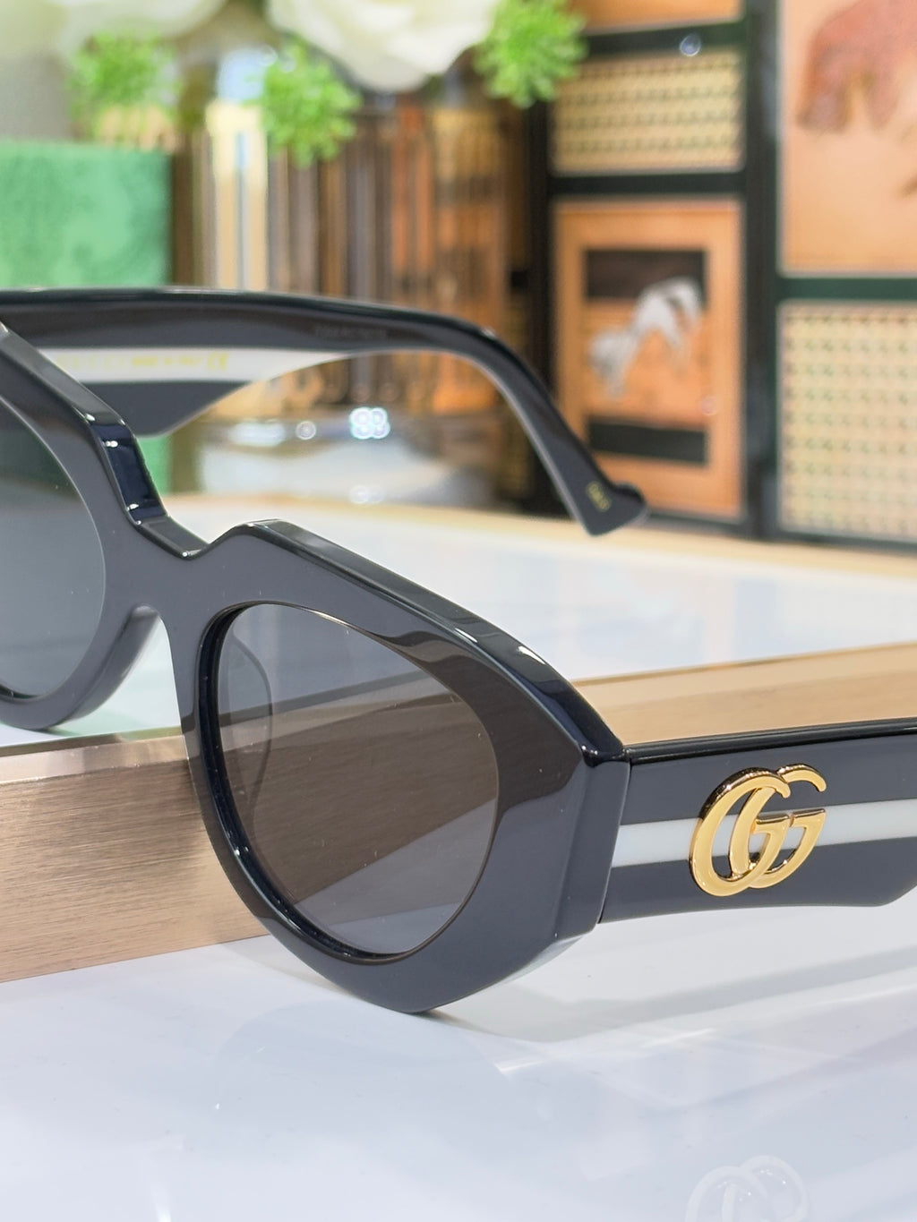 Close-up sunglasses with black frames and gold GG emblem on the temple, dark tinted lens.