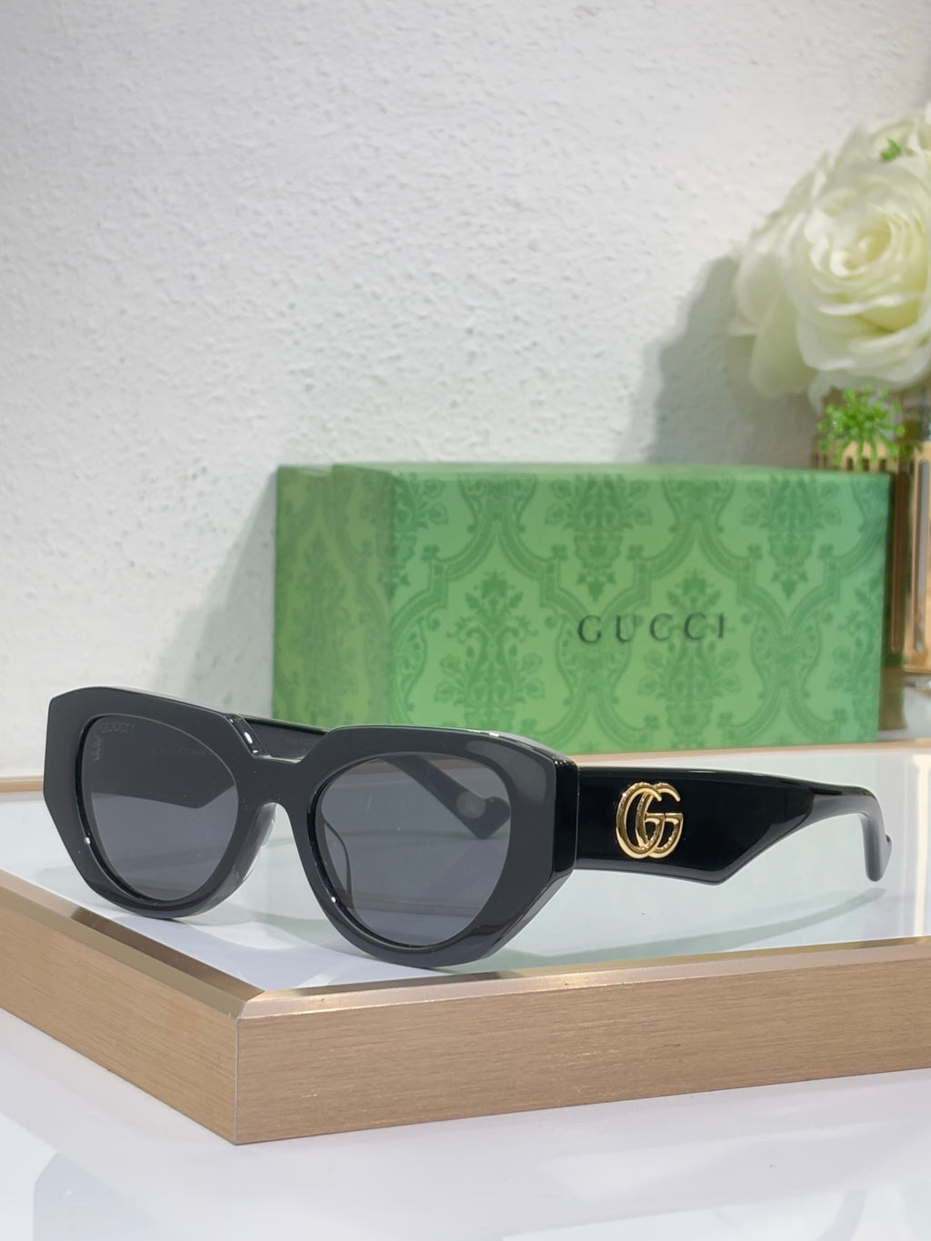 Sunglasses with black frames, dark lenses, and a gold GG emblem on the temple.