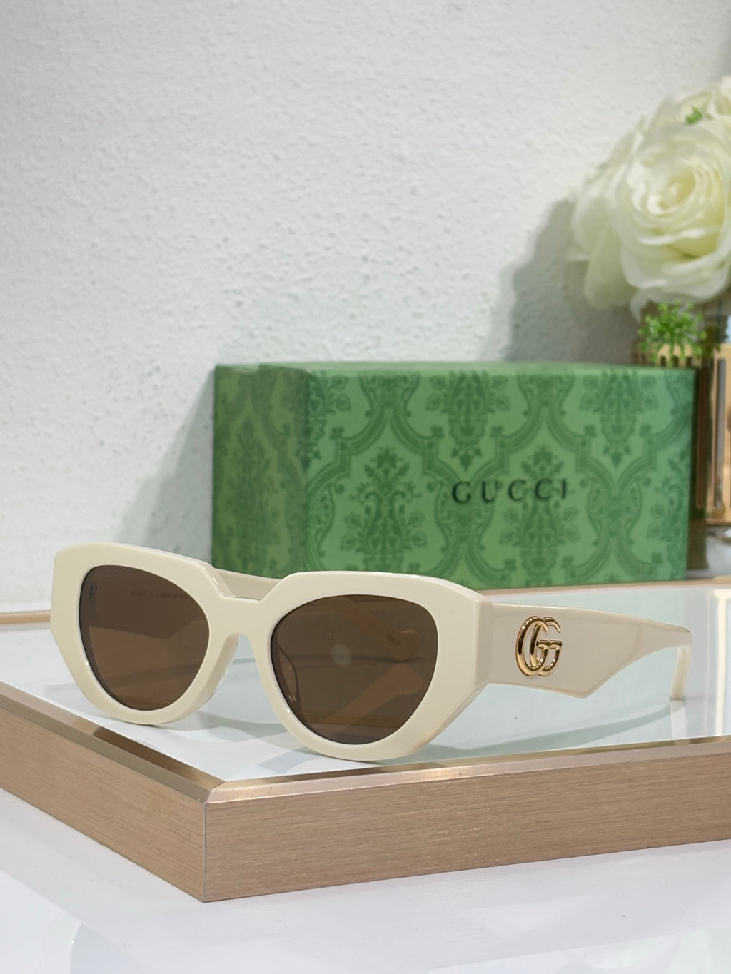 Sunglasses with cream frames, brown-tinted lenses, and a gold GG emblem on the temple.