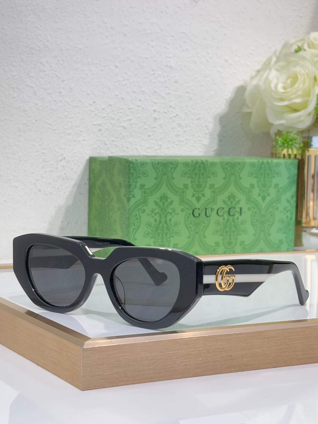 Sunglasses with black frames, dark lenses, and gold GG logo details on the temple.