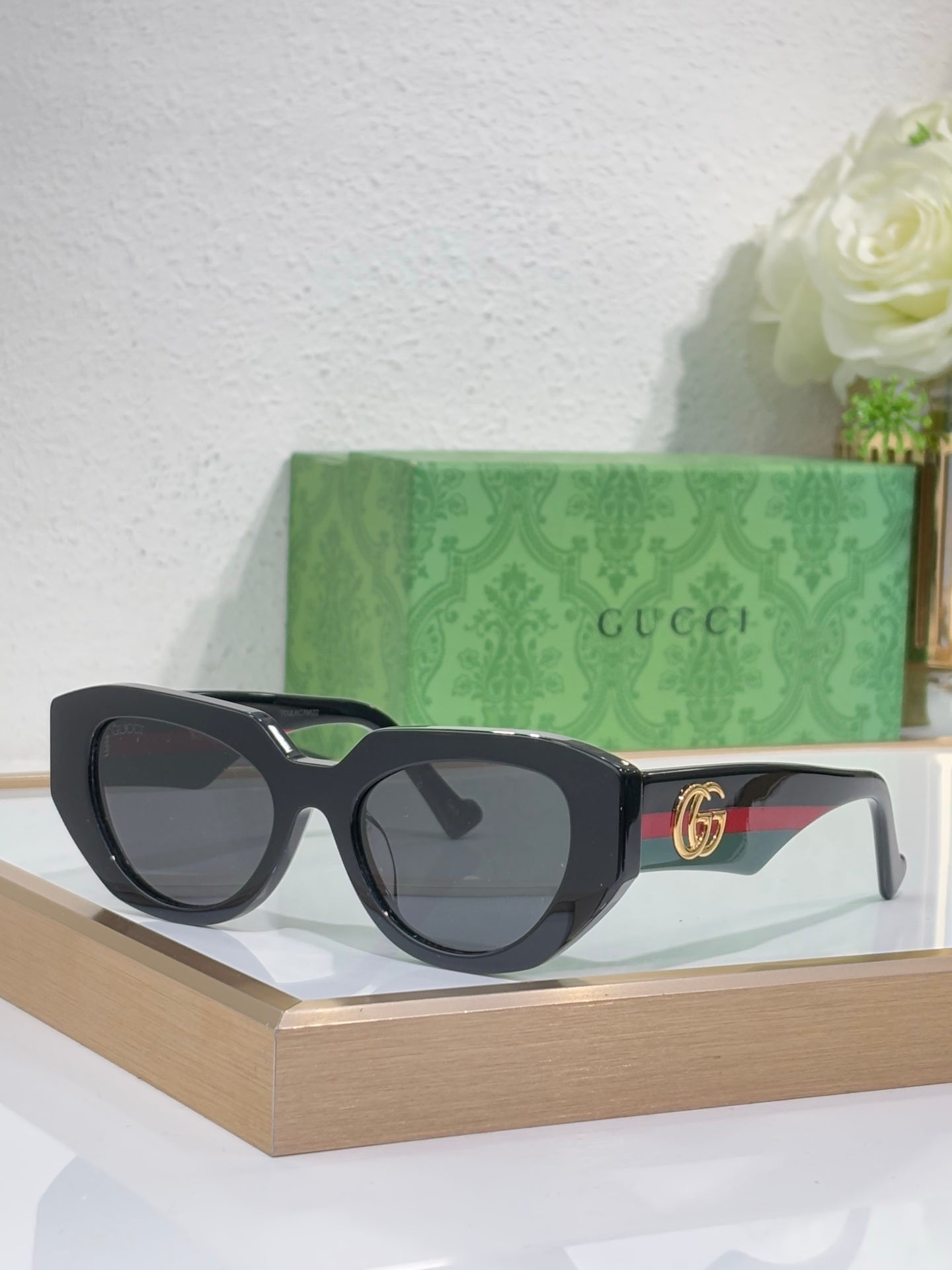 Sunglasses with black frames, green temple accents, and dark lenses with a gold GG emblem.