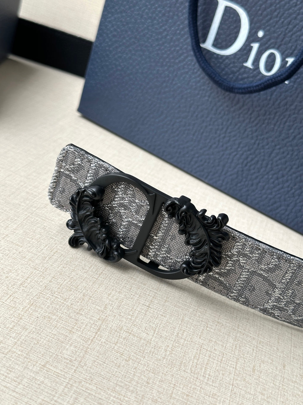 Belt buckle detail with black ornate frame on silver-gray monogram strap