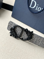 Belt buckle detail with black ornate frame on silver-gray monogram strap