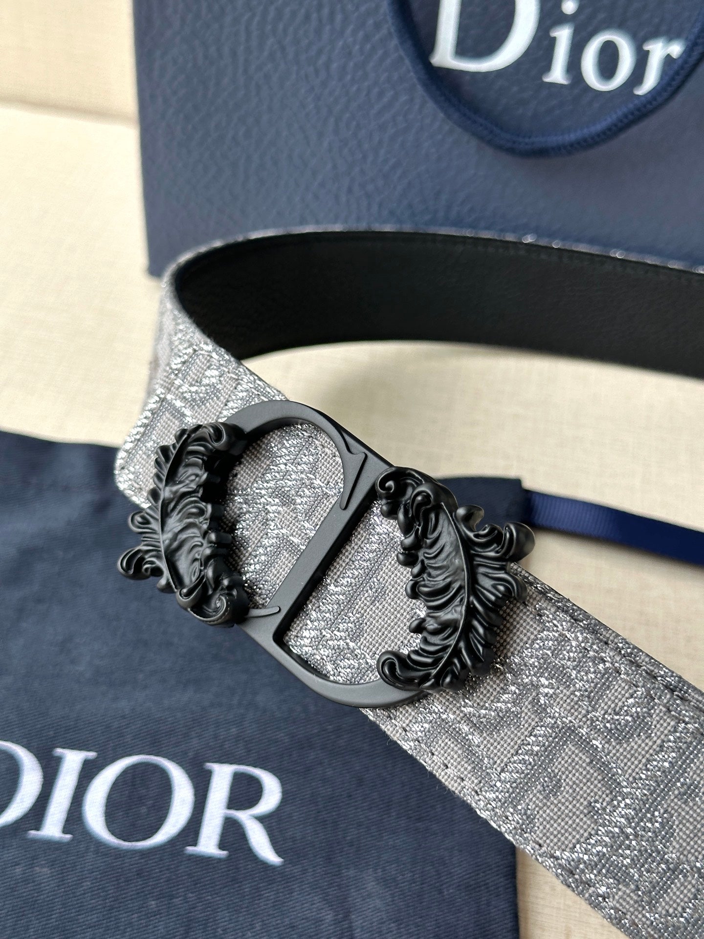 Belt buckle detail with black metal scrollwork on silver-gray strap