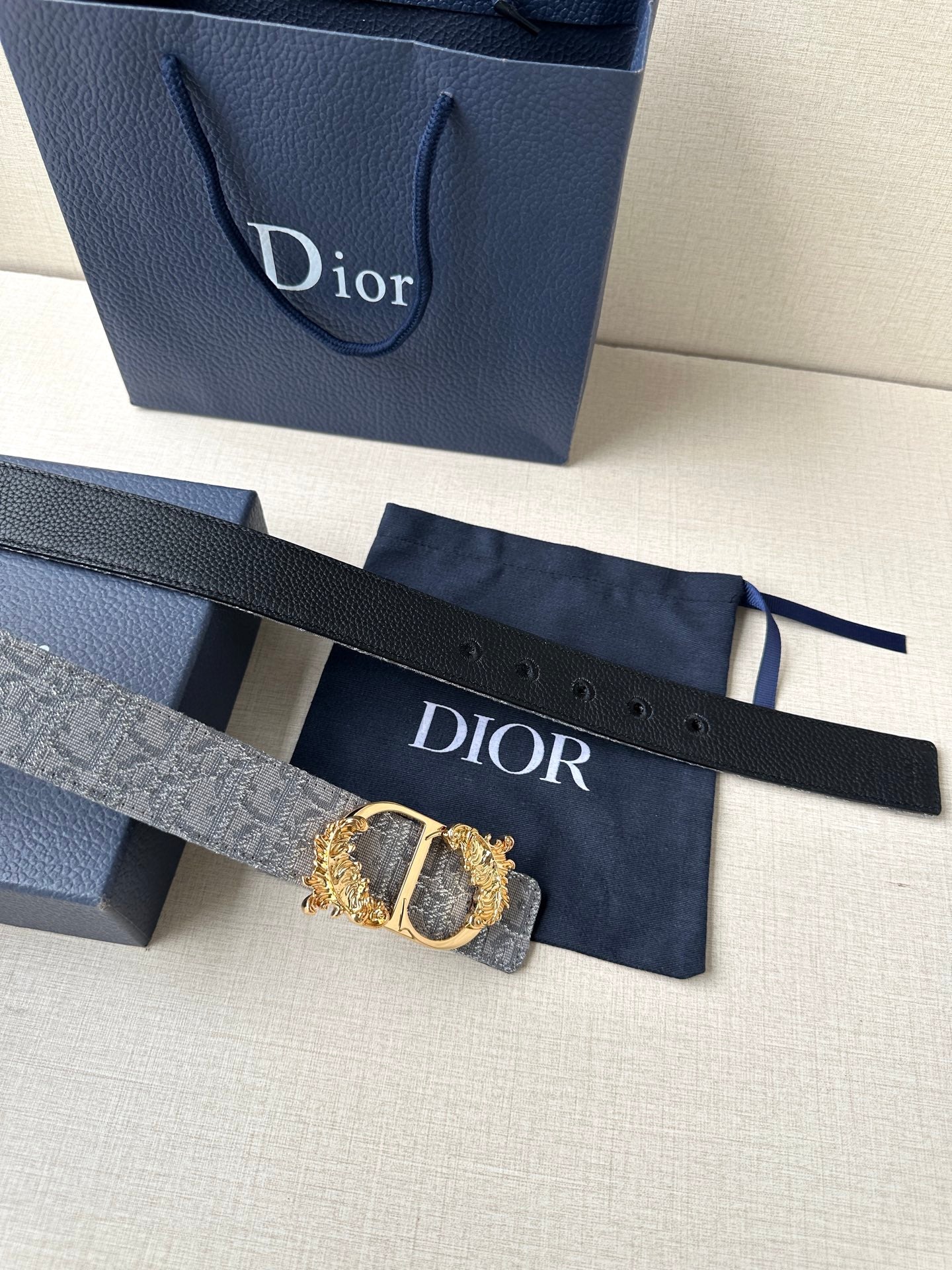 Dior belt strap with cut holes and gold-toned buckle hardware, flat on display.