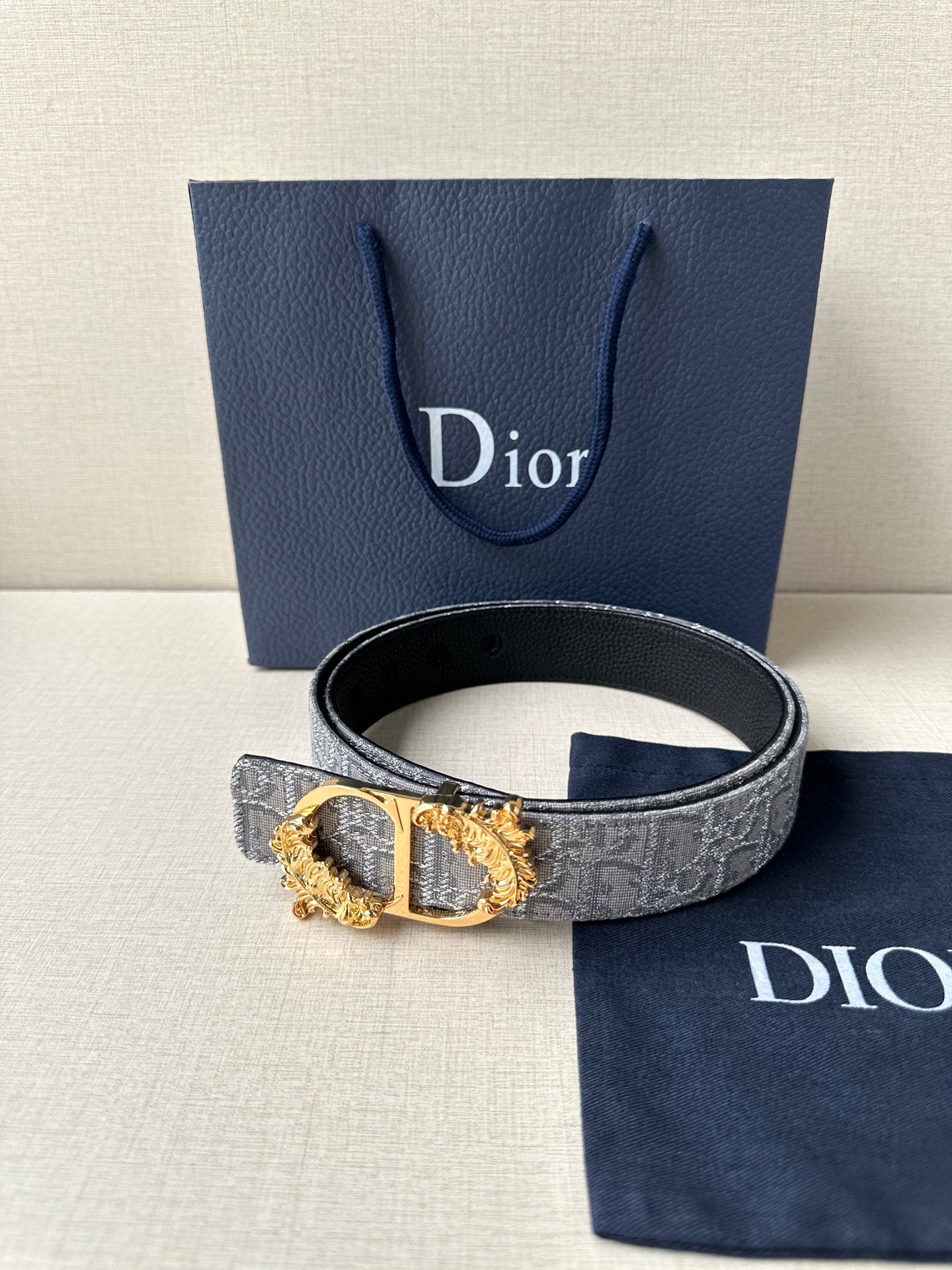Dior logo-print belt with silver-gray strap and gold-toned ornate buckle.