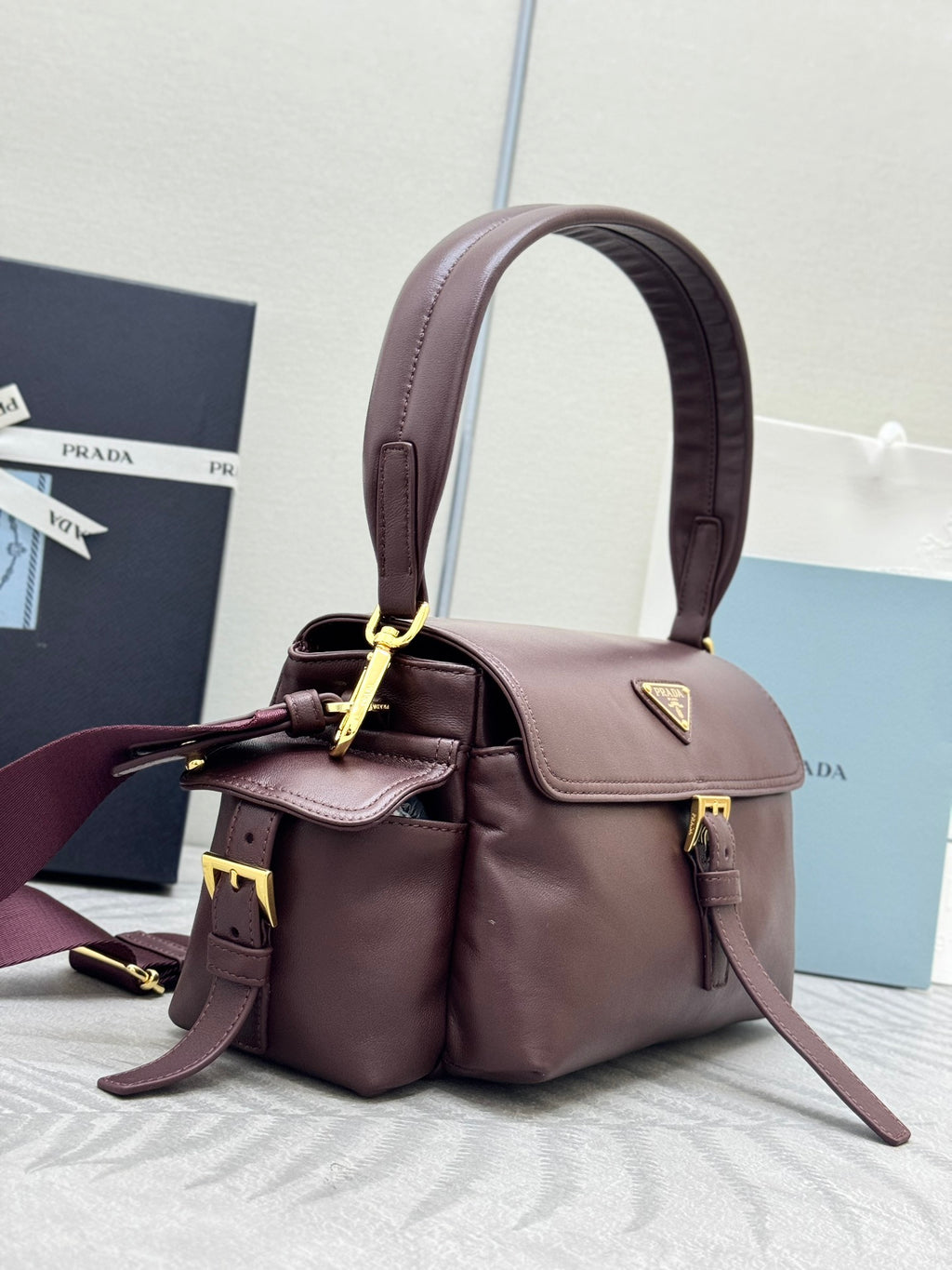 Burgundy Prada handbag with top handle, front flap and gold hardware with strap