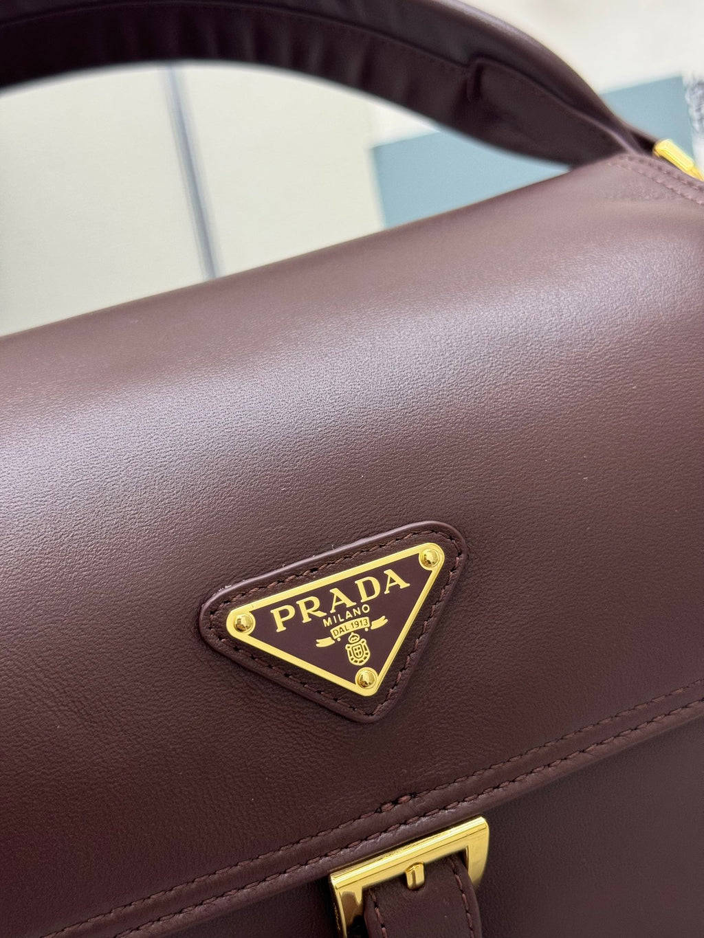 Burgundy Prada bag with gold triangle logo patch on flap