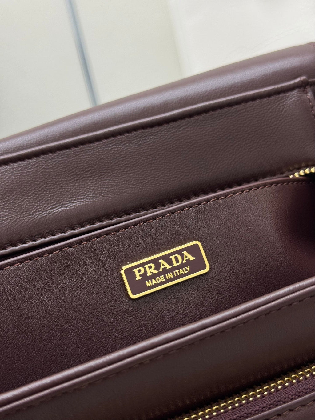 Burgundy Prada bag with gold Made in Italy logo plate on seam