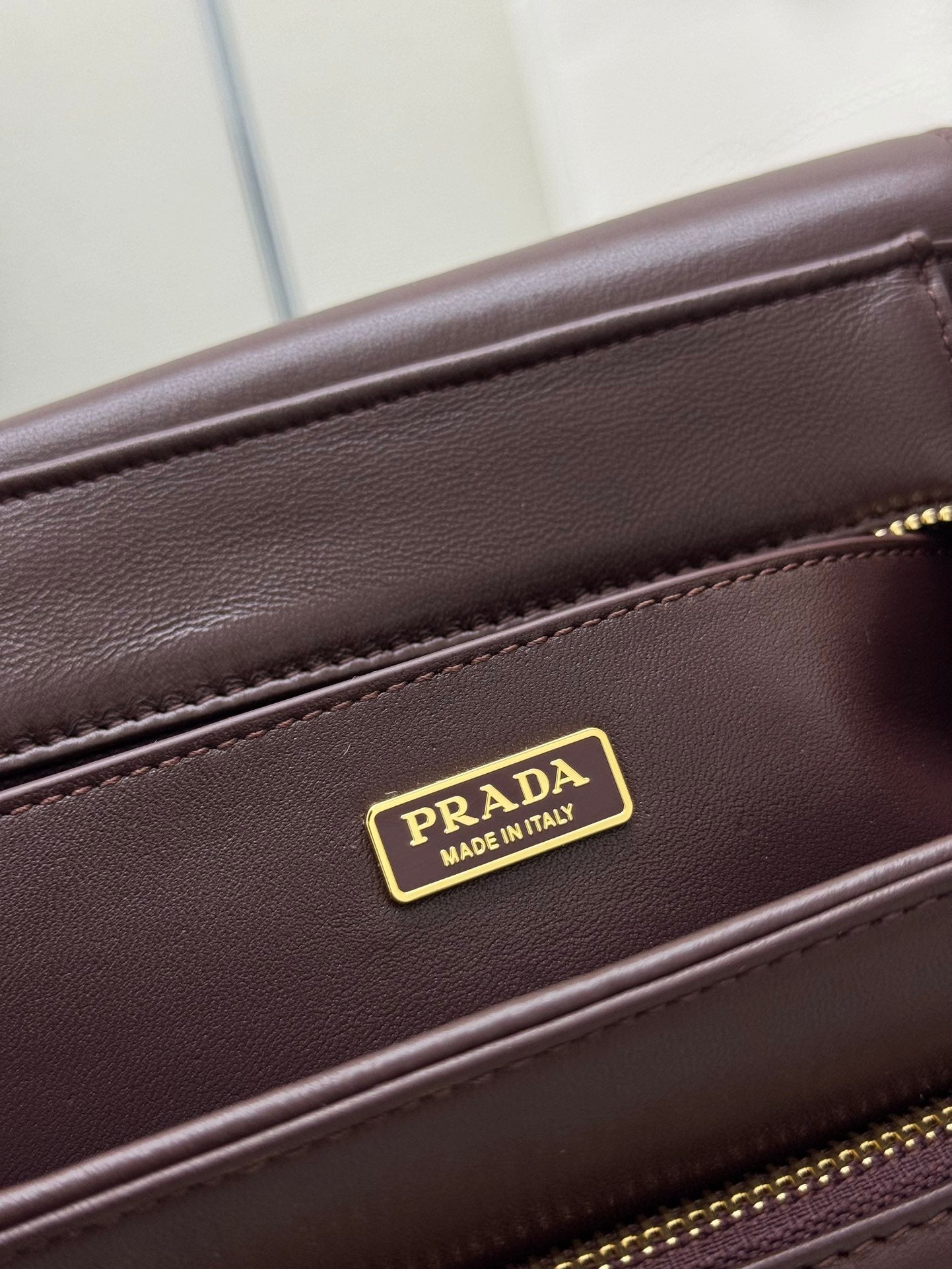Burgundy Prada bag with gold Made in Italy logo plate on seam
