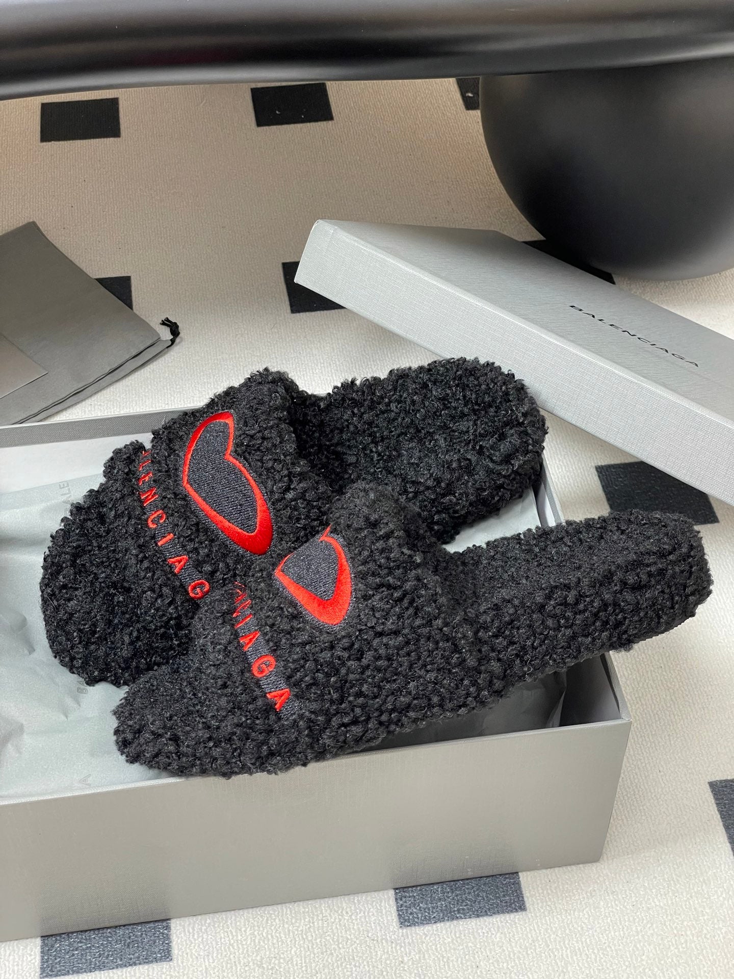 Black teddy-fleece slide sandals with red heart logos in an open shoebox