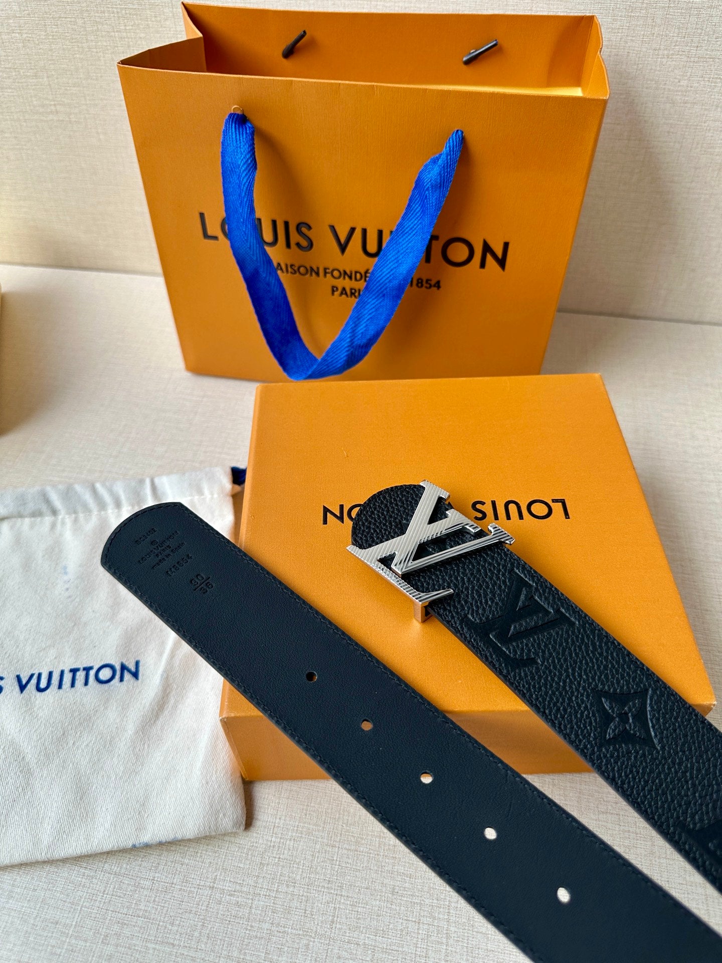 Louis Vuitton belt and strap end with holes; dark textured leather with LV branding