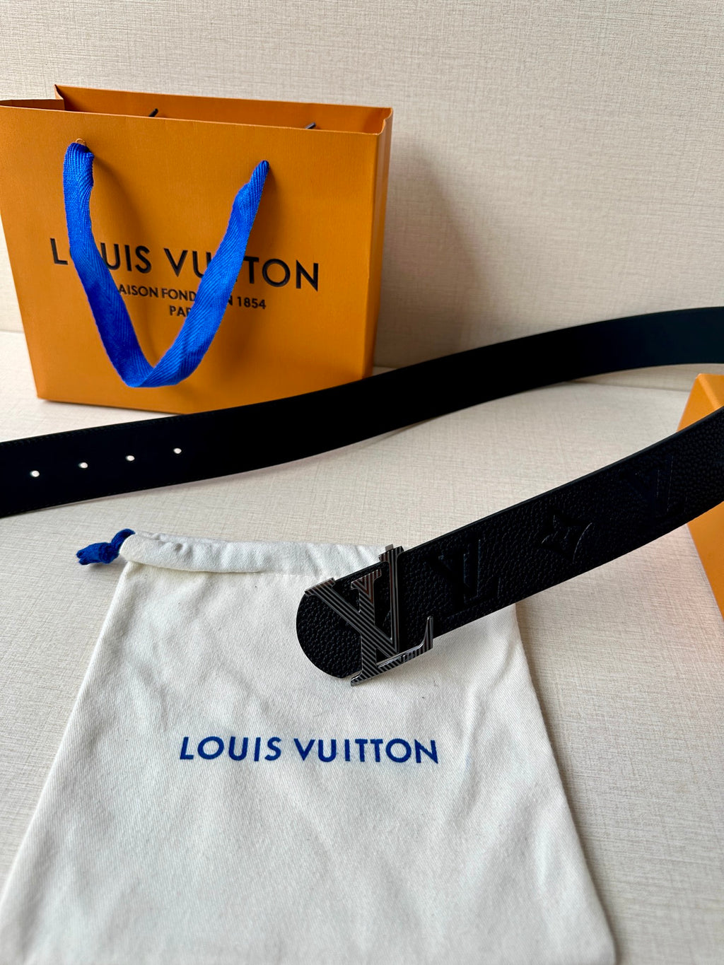 Louis Vuitton belt with buckle and rows of holes on dark leather, on dust bag