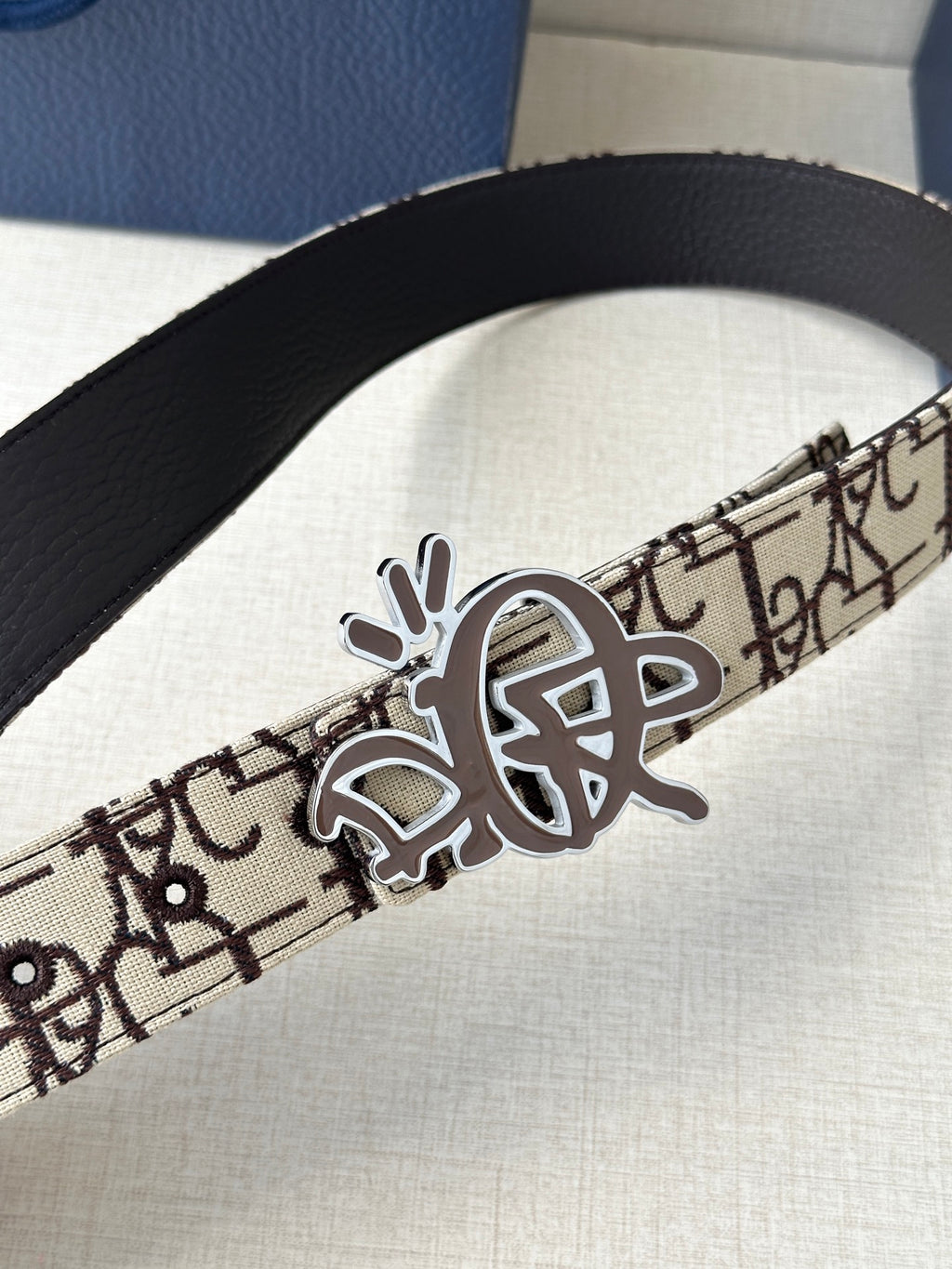 Dior belt close-up: beige logo strap with black inner, gold-toned clasp